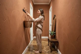 Entrée de location peinte en terracotta chaud avec crochets noirs, parquet en chevrons et plante verte pour une déco simple et économique