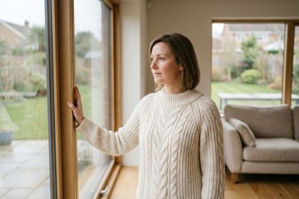 Femme devant une fenêtre double vitrage moderne dans un salon confortable, illustrant le confort thermique apporté par des fenêtres de qualité